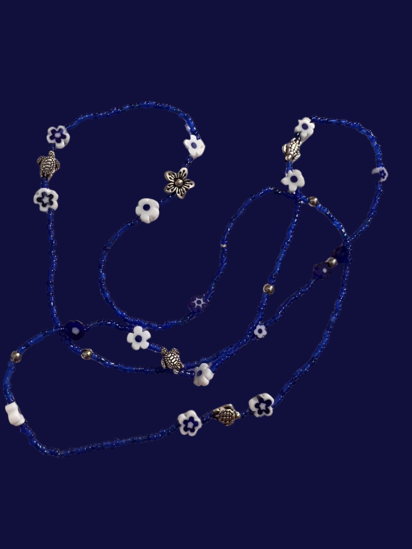 Blue wasitbeads with white flowers and silver metal turtles on a light background