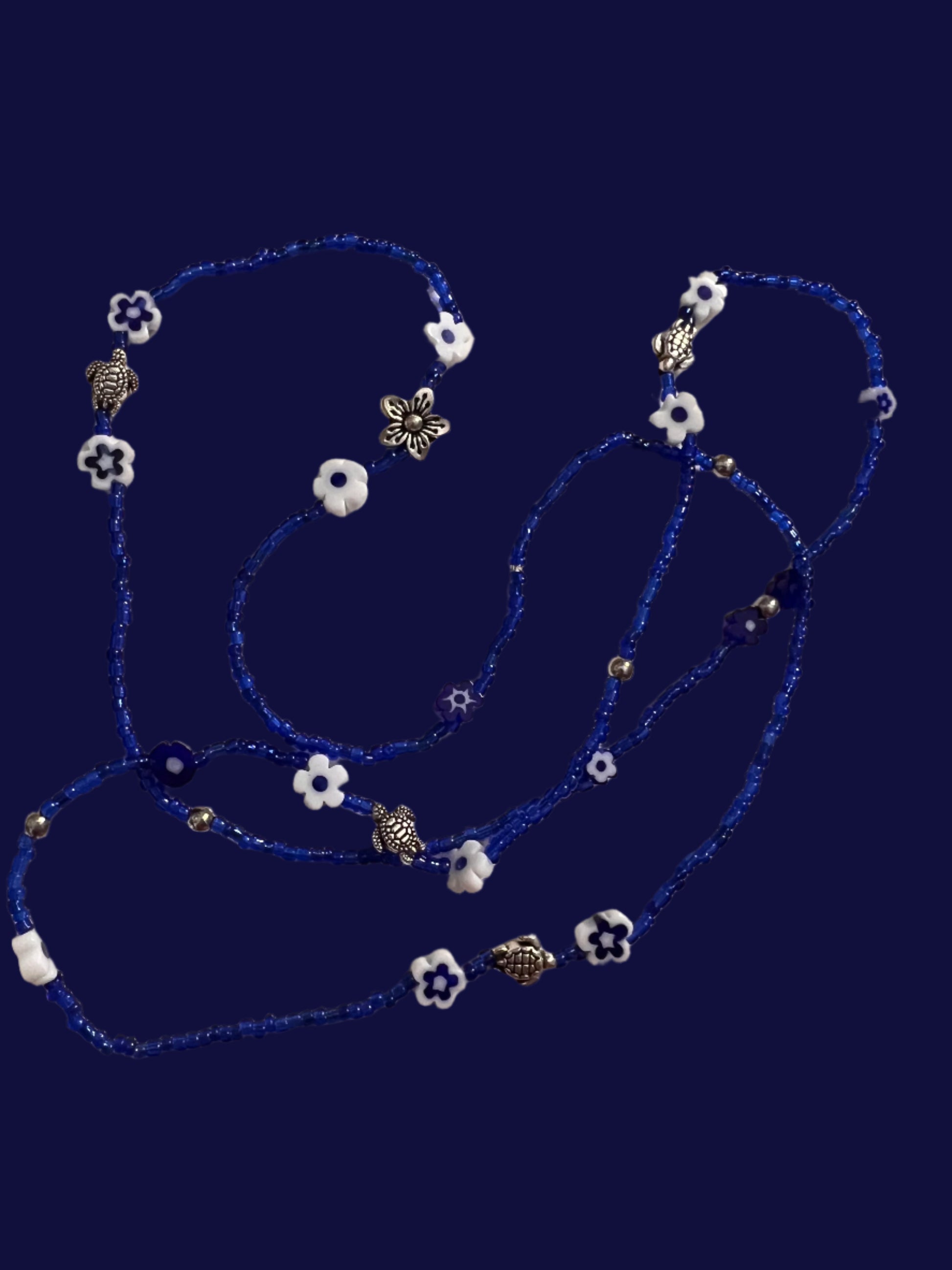 Blue wasitbeads with white flowers and silver metal turtles on a light background