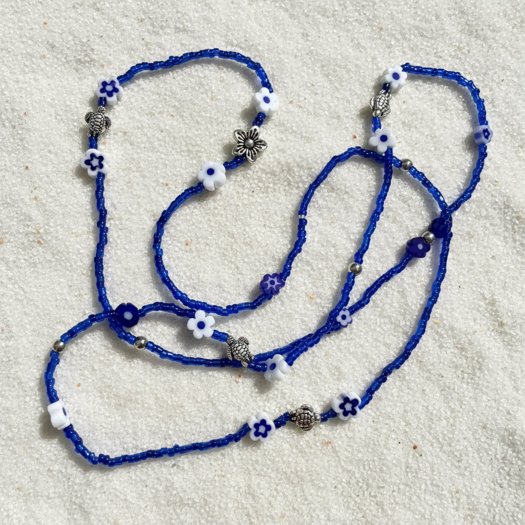 Blue wasitbeads with white flowers and silver metal turtles on a light background