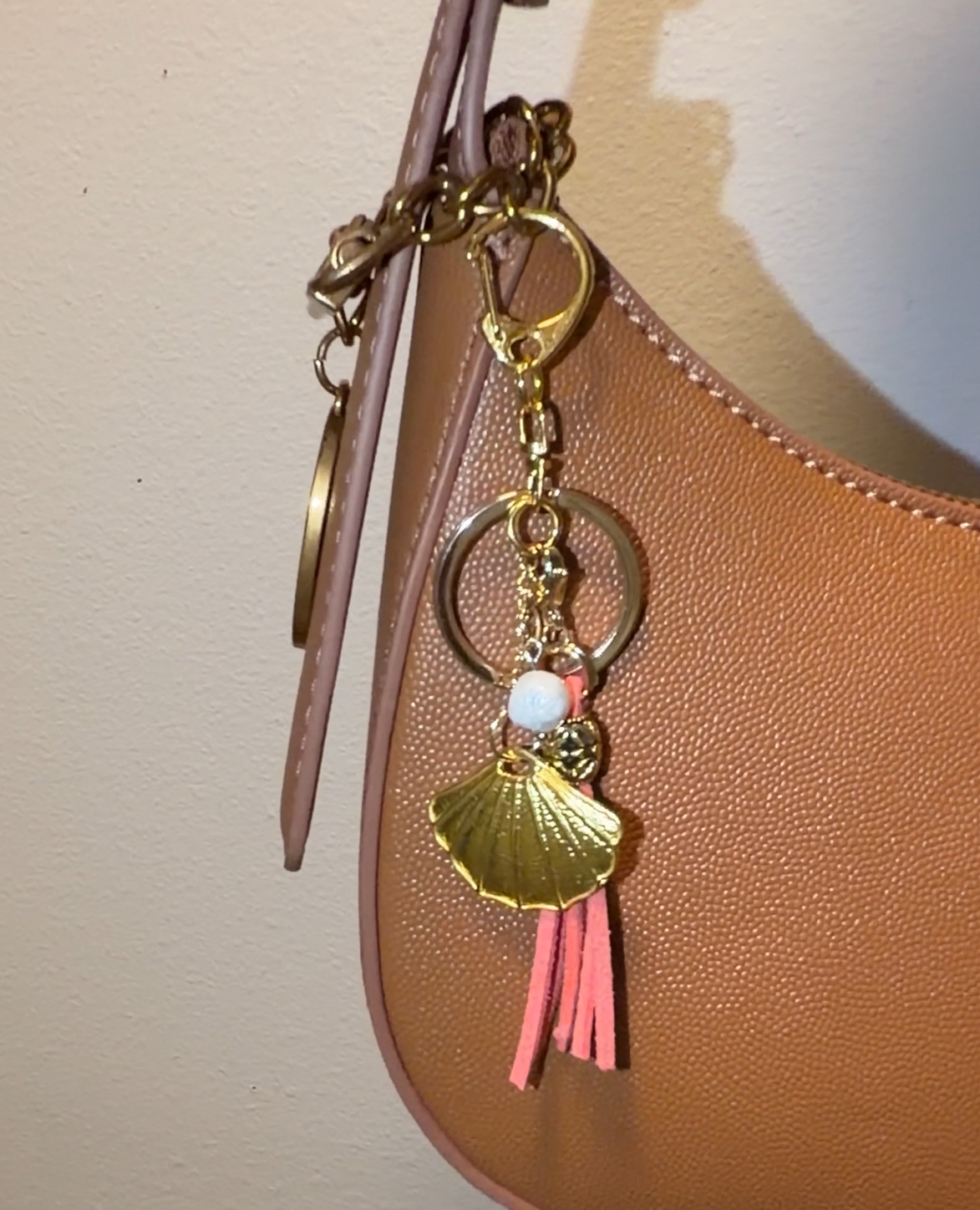 Handbag with decorative charm featuring a peach tassel, gold shell, and freshwater pearl.