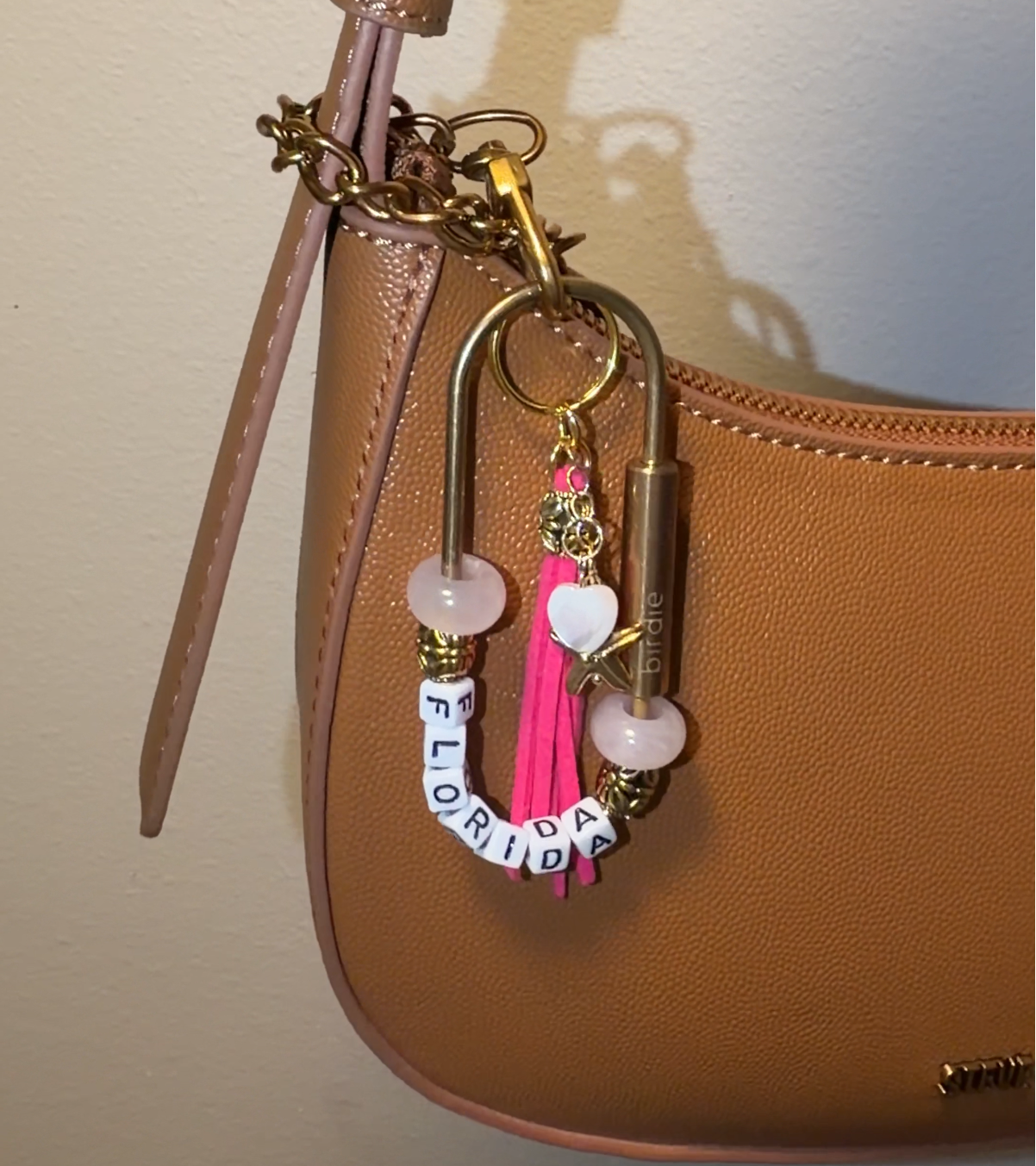 Handbag with decorative charm featuring a dark pink tassel, gold starfish, heart charm