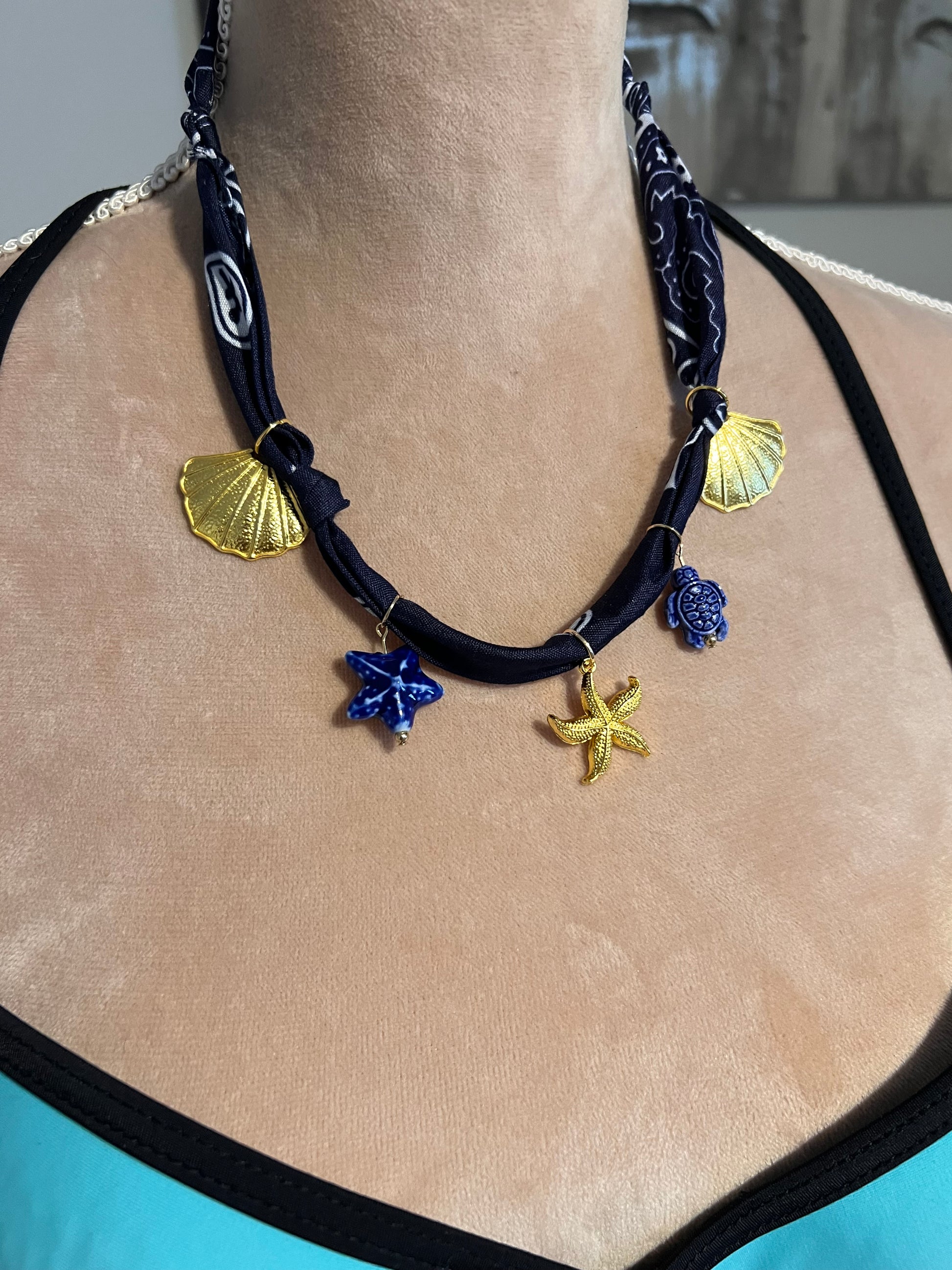 navy bandana necklace with gold charms on a beige surface mannequin 