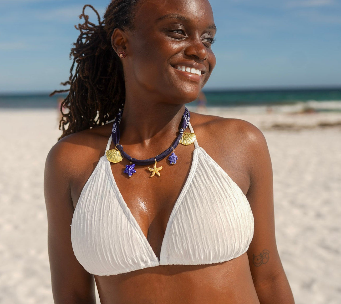 Woman in a white bikini standing on a beach with ocean and sky in the background