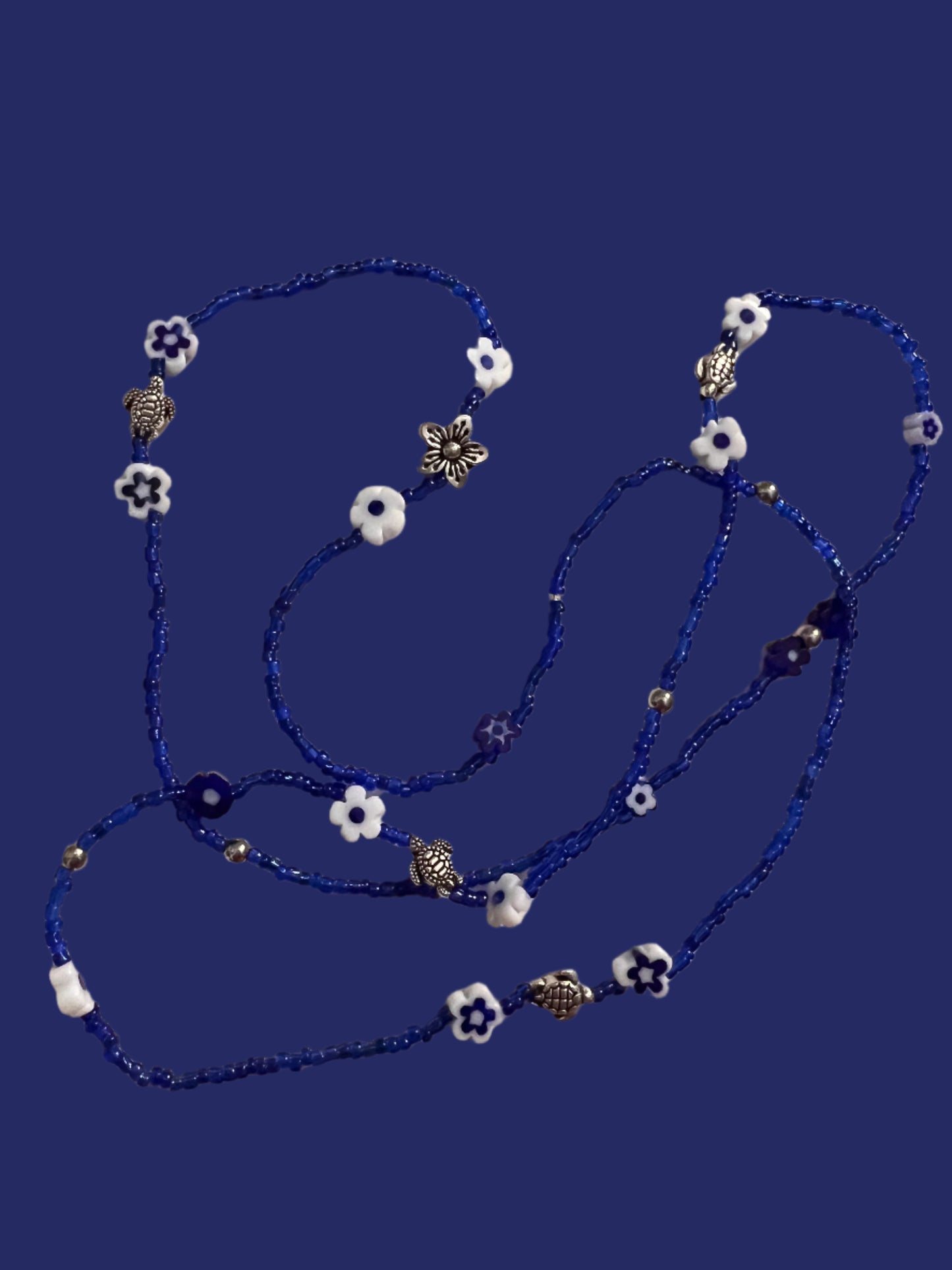 Blue waistbeadswith white flowers and silver turtles on a light background