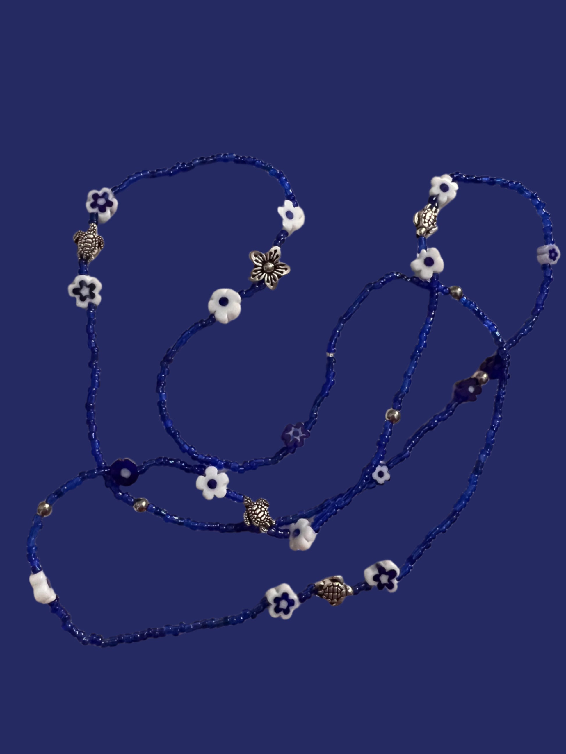 Blue waistbeadswith white flowers and silver turtles on a light background
