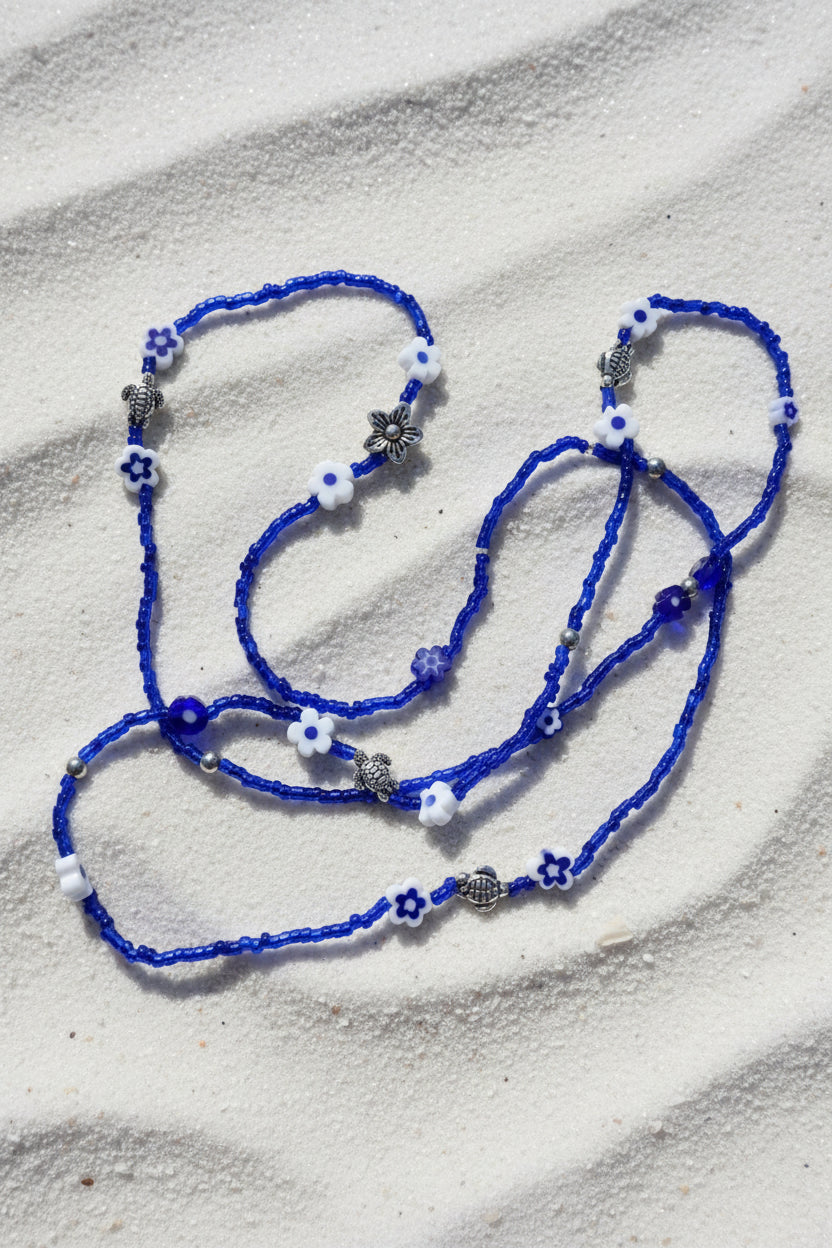 Blue waistbeadswith white flowers and silver turtles on a light background