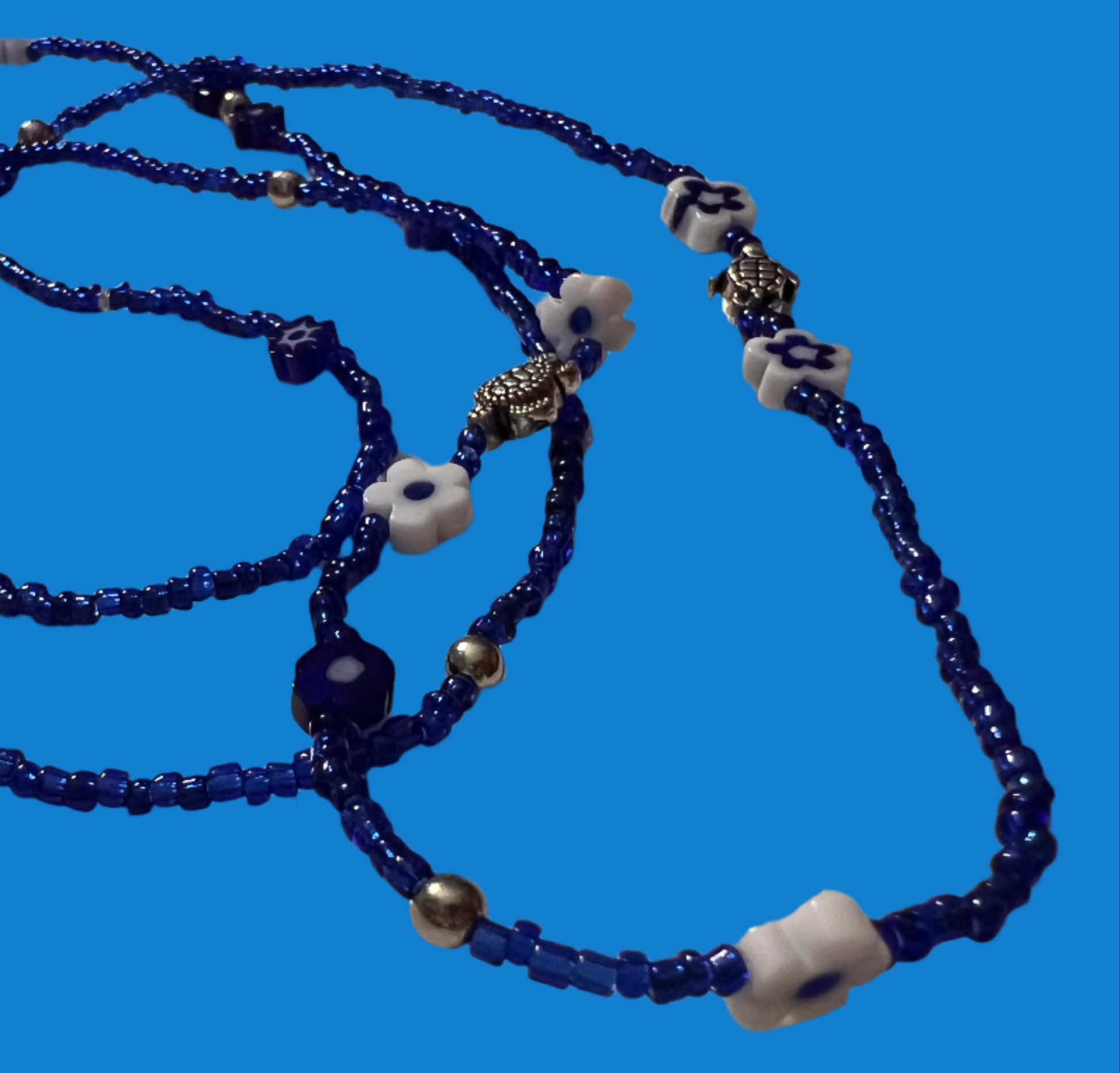 Blue waistbeads with white flower-shaped beads on a light gray background
