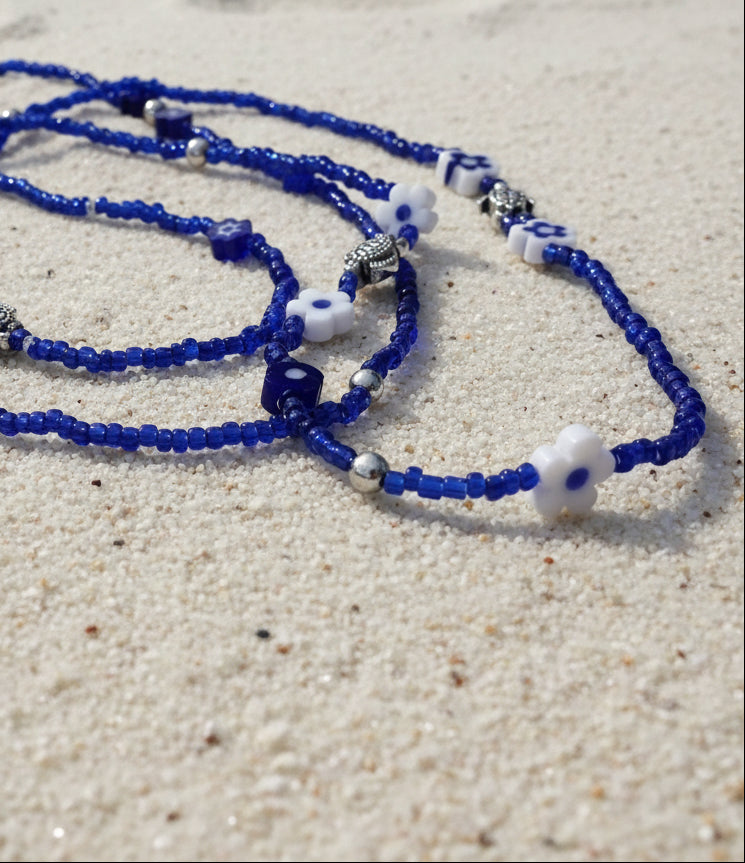 Blue waistbeads with white flower-shaped beads on a light gray background
