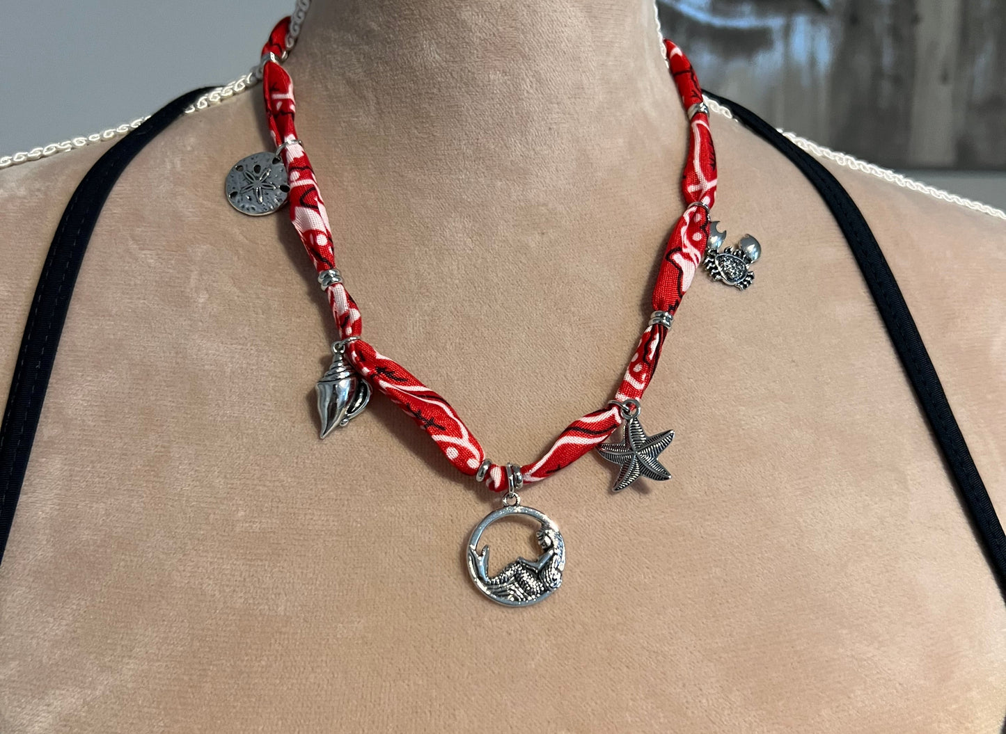 Red bandana necklace with silver charms on a person's neck against a blurred background