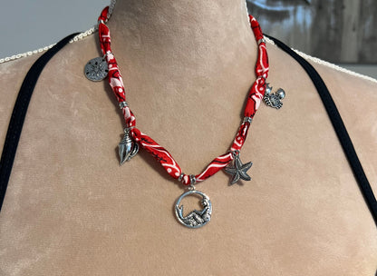 Red bandana necklace with silver charms on a person's neck against a blurred background
