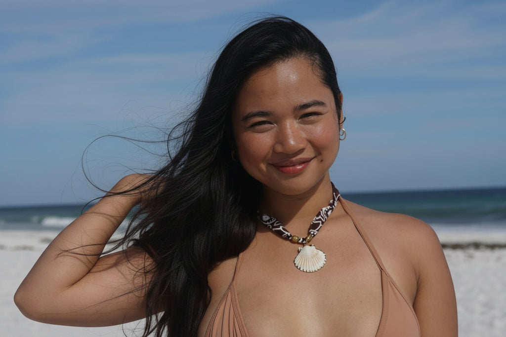 A woman posing on a white sand beach wearing a beige string bikini and gabi decor studio bandana necklace