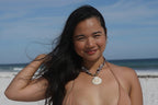 A woman posing on a white sand beach wearing a beige string bikini and gabi decor studio bandana necklace