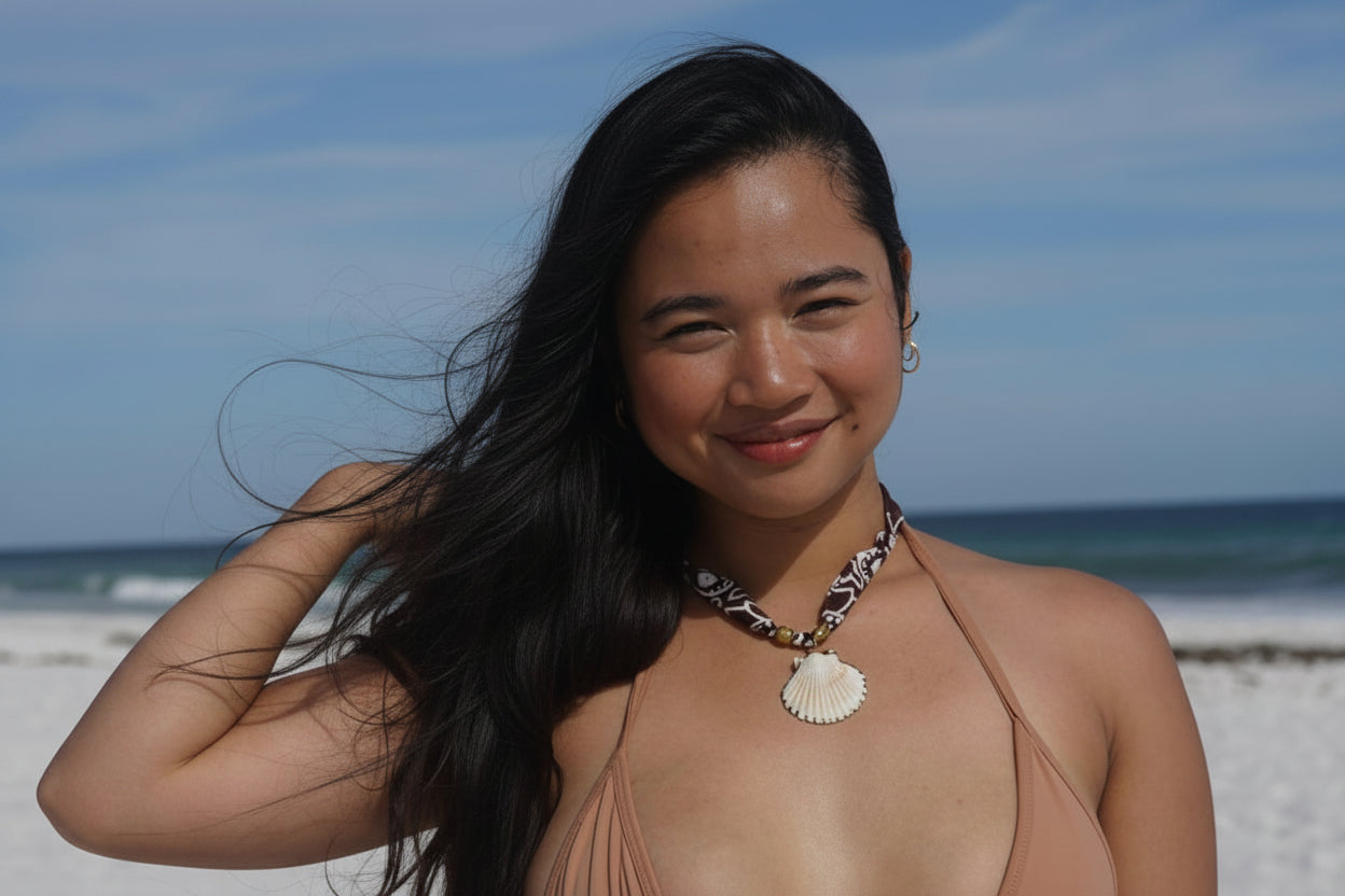 A woman posing on a white sand beach wearing a beige string bikini and gabi decor studio bandana necklace