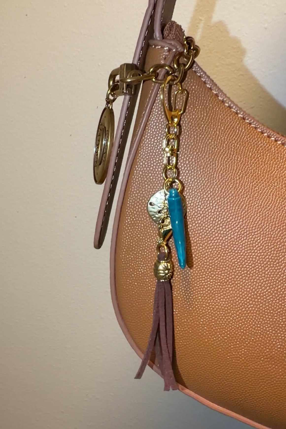 Handbag with decorative charm featuring a brown tassle, gold sand dollar, porcelain pepper charm