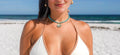 Woman in a white bikini standing on a sandy beach with ocean and blue sky in the background