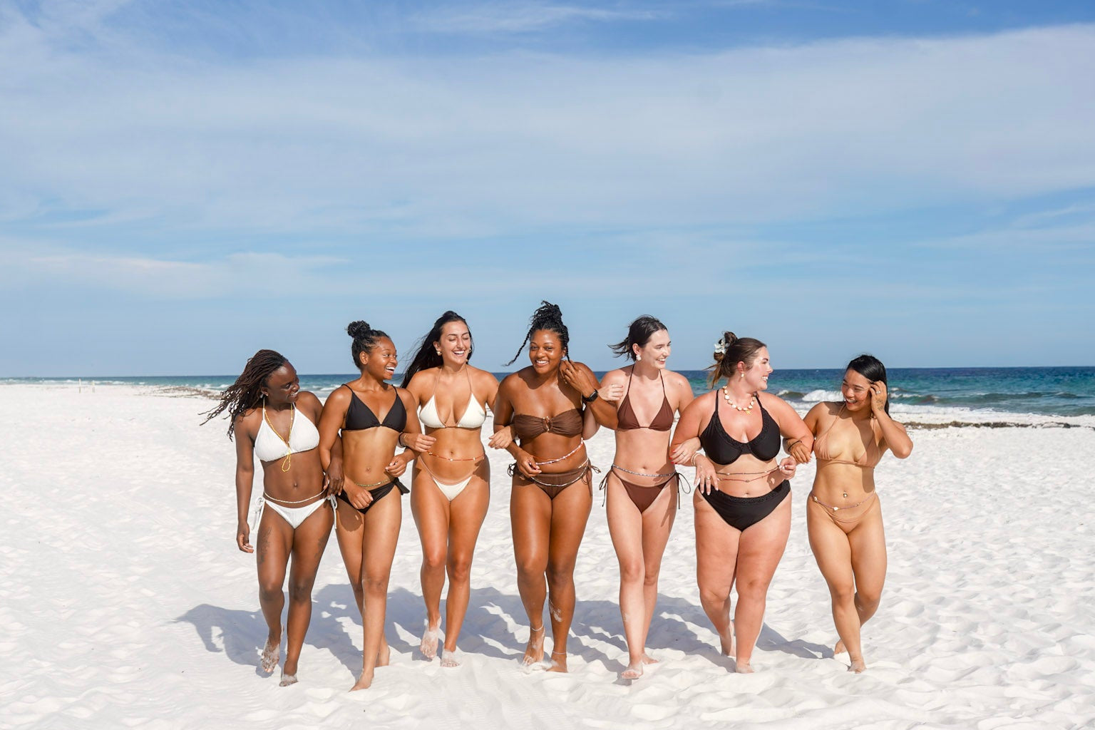 Group of women in swimsuits standing on a sandy beach with ocean in the background