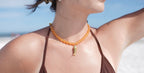 Woman wearing an orange beaded necklace with a pendant on a beach.