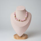 A pink beaded bracelet with small gold starfish charms displayed on a pink jewelry bust.