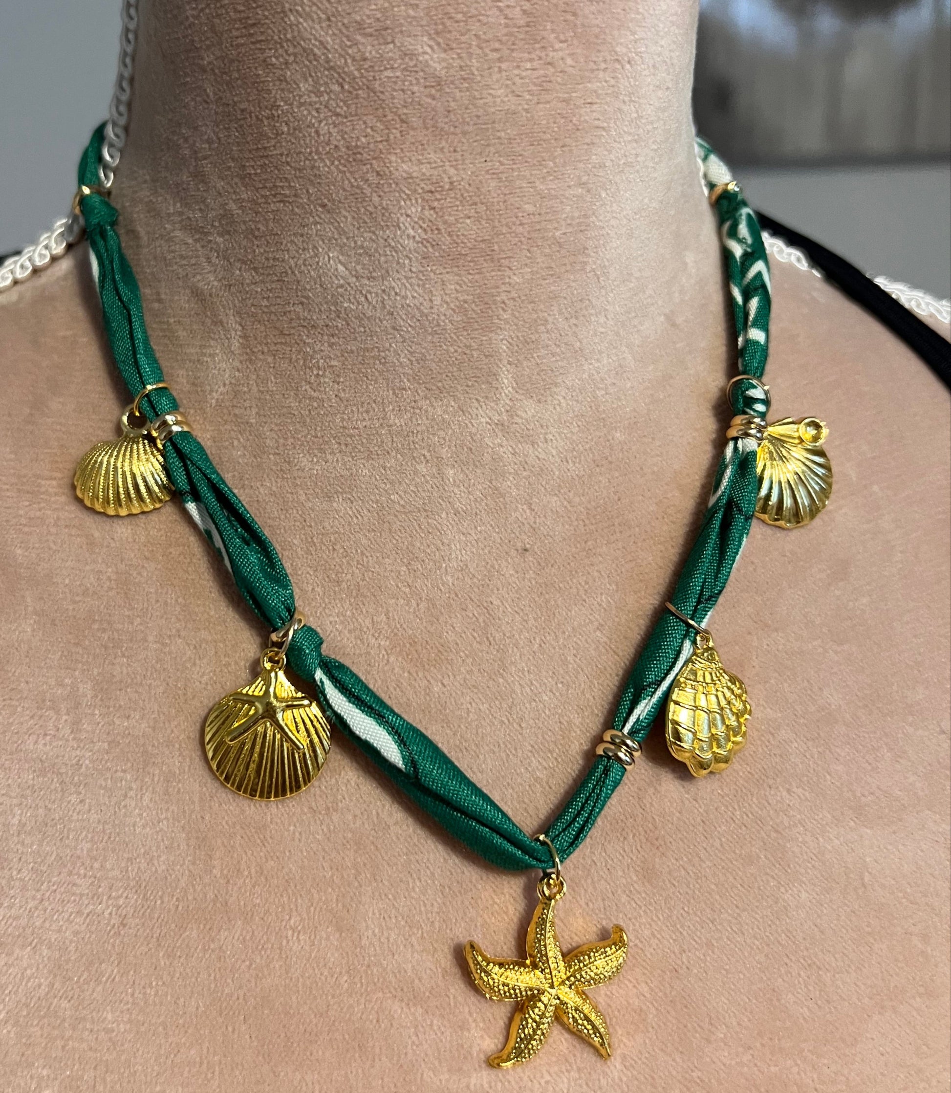 Green bandana necklace with gold starfish and shell charms on a neck.
