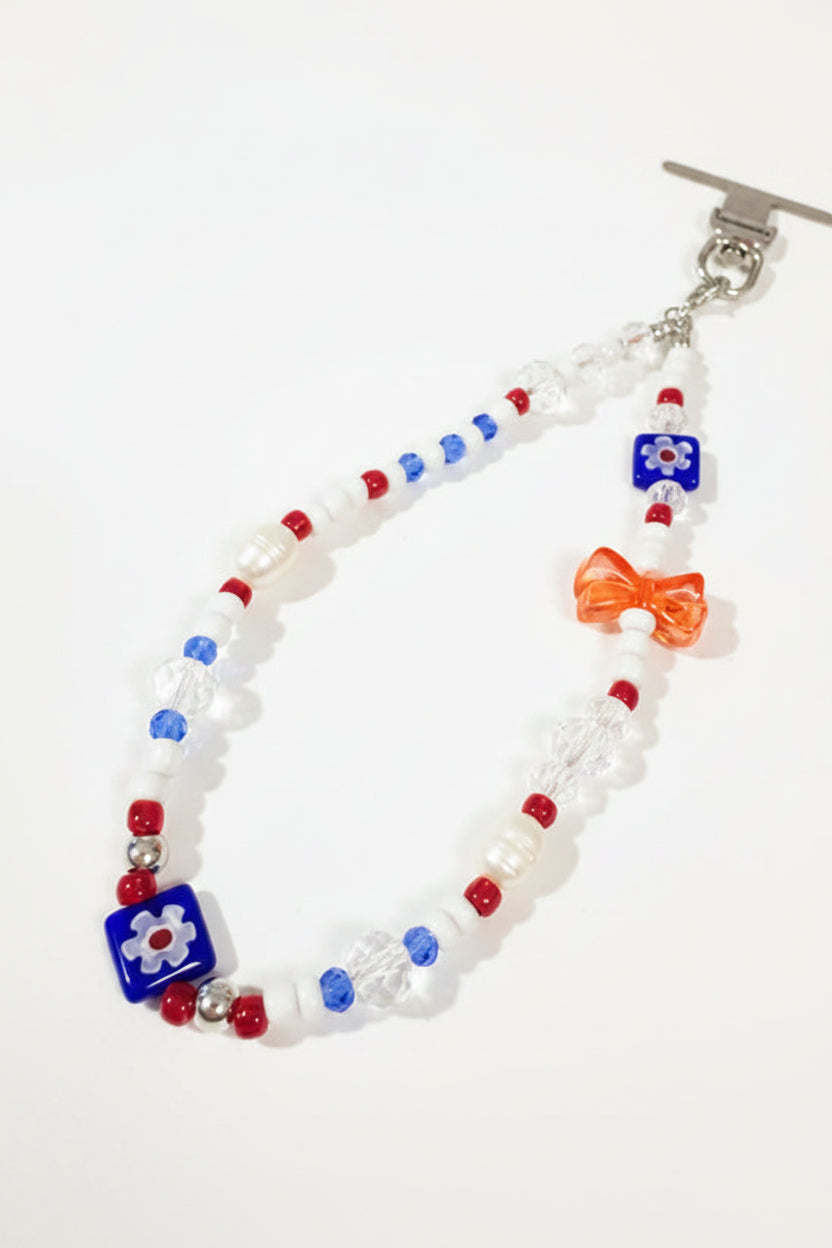 A beaded bracelet with a silver toggle clasp, featuring white faux-pearl beads, red and blue accent beads, clear faceted beads, and a small red bow charm
