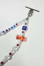 A beaded wristlet with a silver-toned toggle clasp, featuring white beads, a blue and red floral bead, a translucent redbow charm, and faceted clear beads