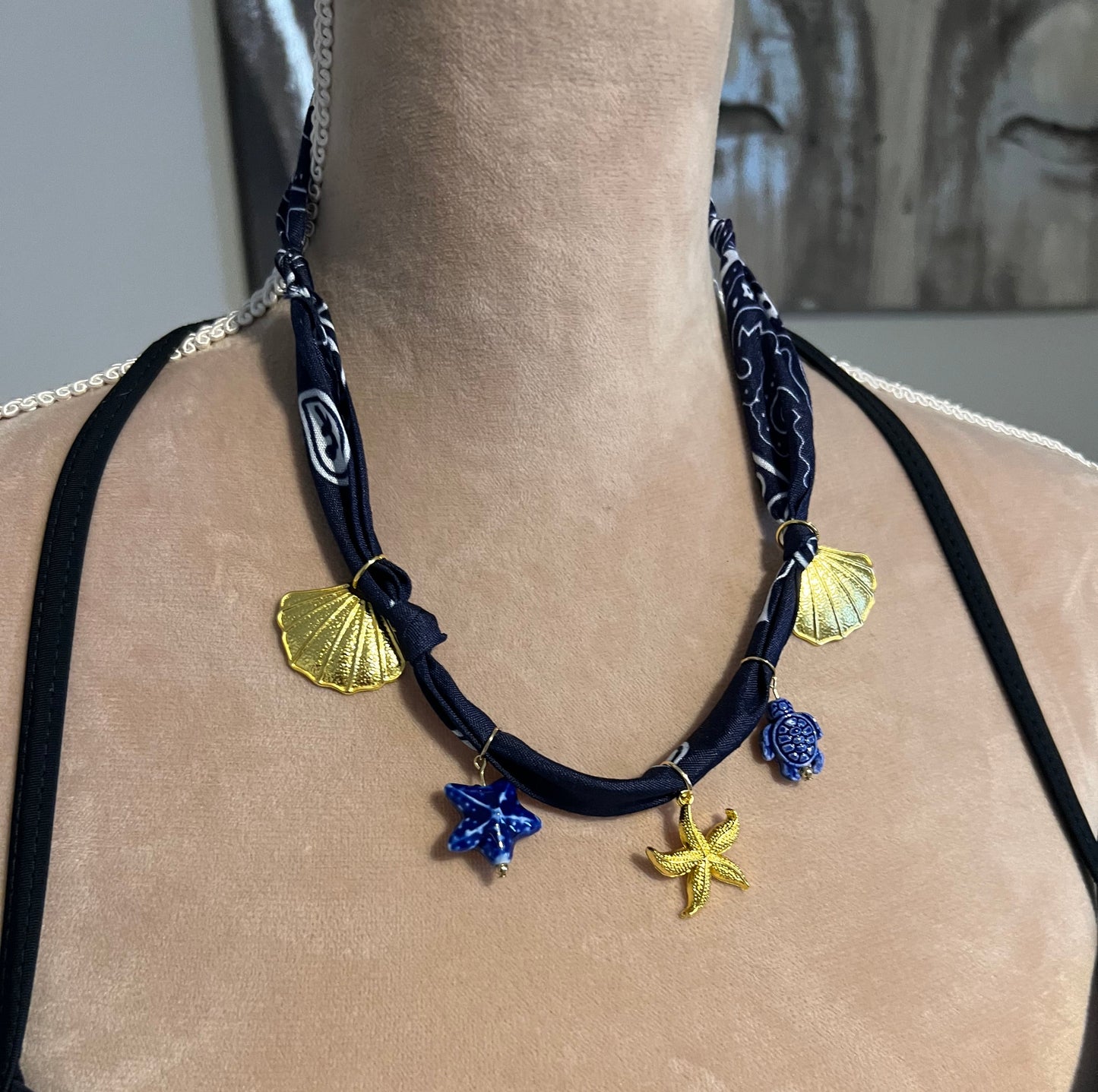 navy bandana necklace with gold charms on a beige surface mannequin 