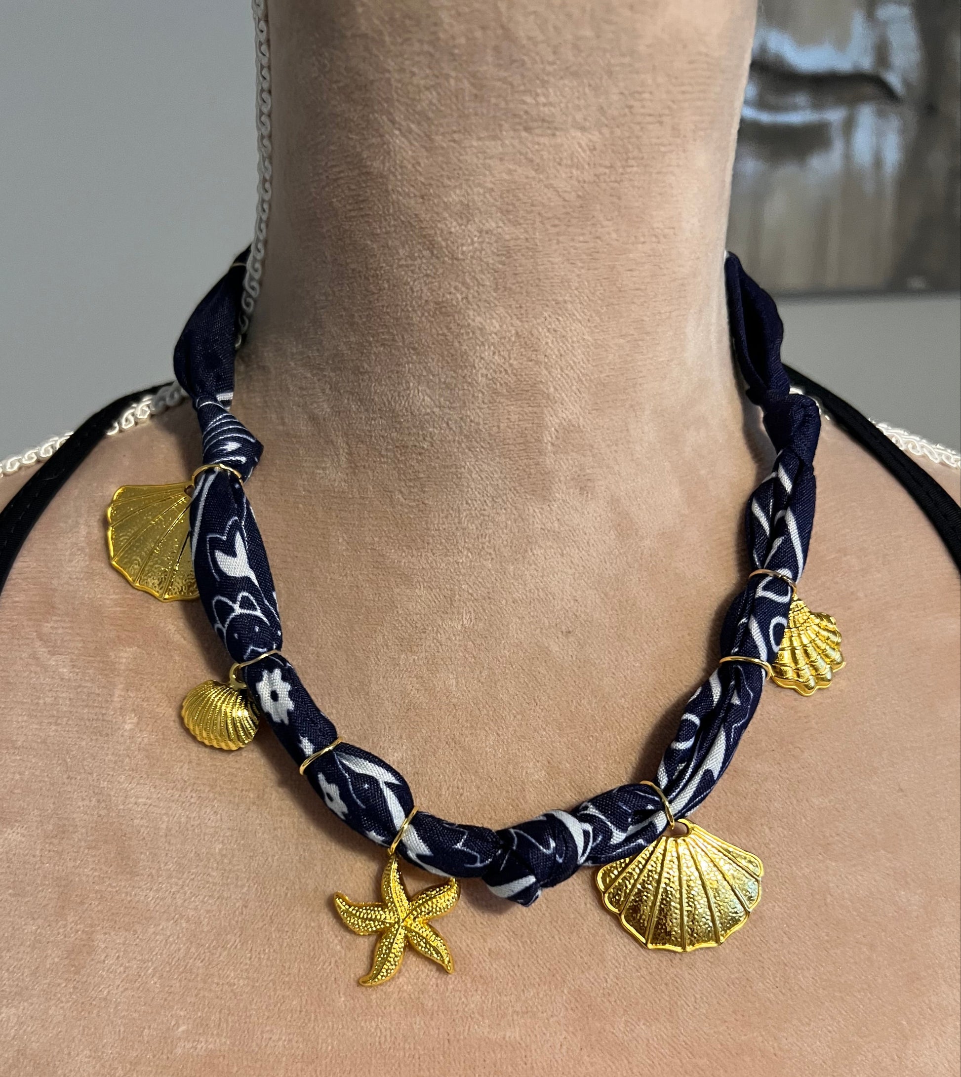 Navy necklace with gold shell and starfish charms on a person's neck.