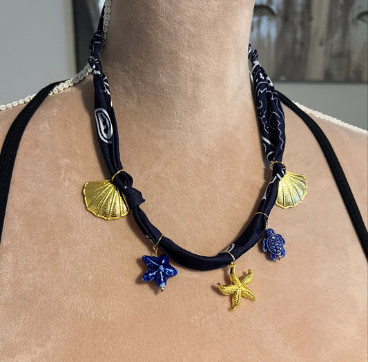 navy bandana necklace with gold charms on a beige surface mannequin 