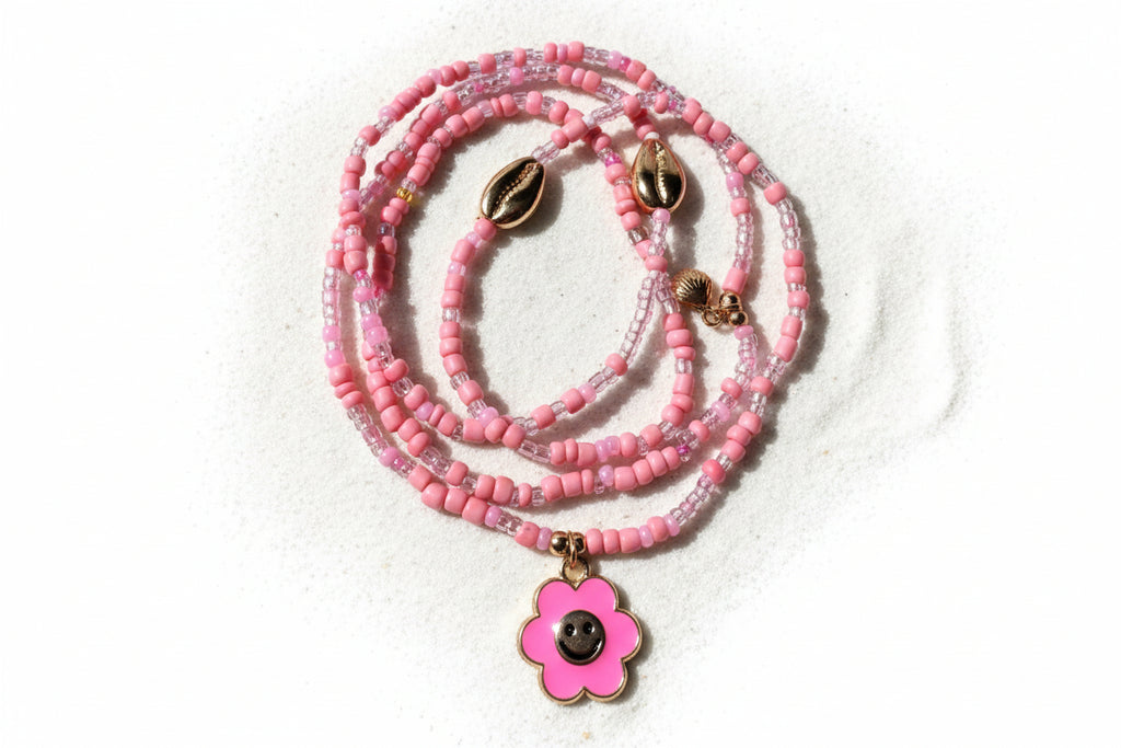 Pink beaded waistbeads with a flower pendant on a wooden surface