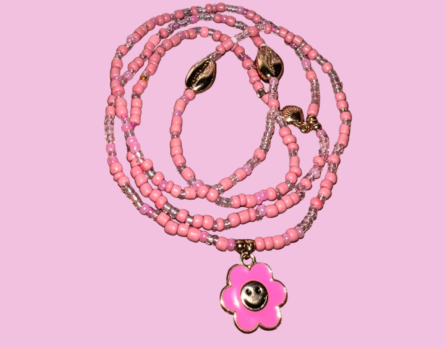 Pink beaded waistbeads with a flower pendant on a wooden surface