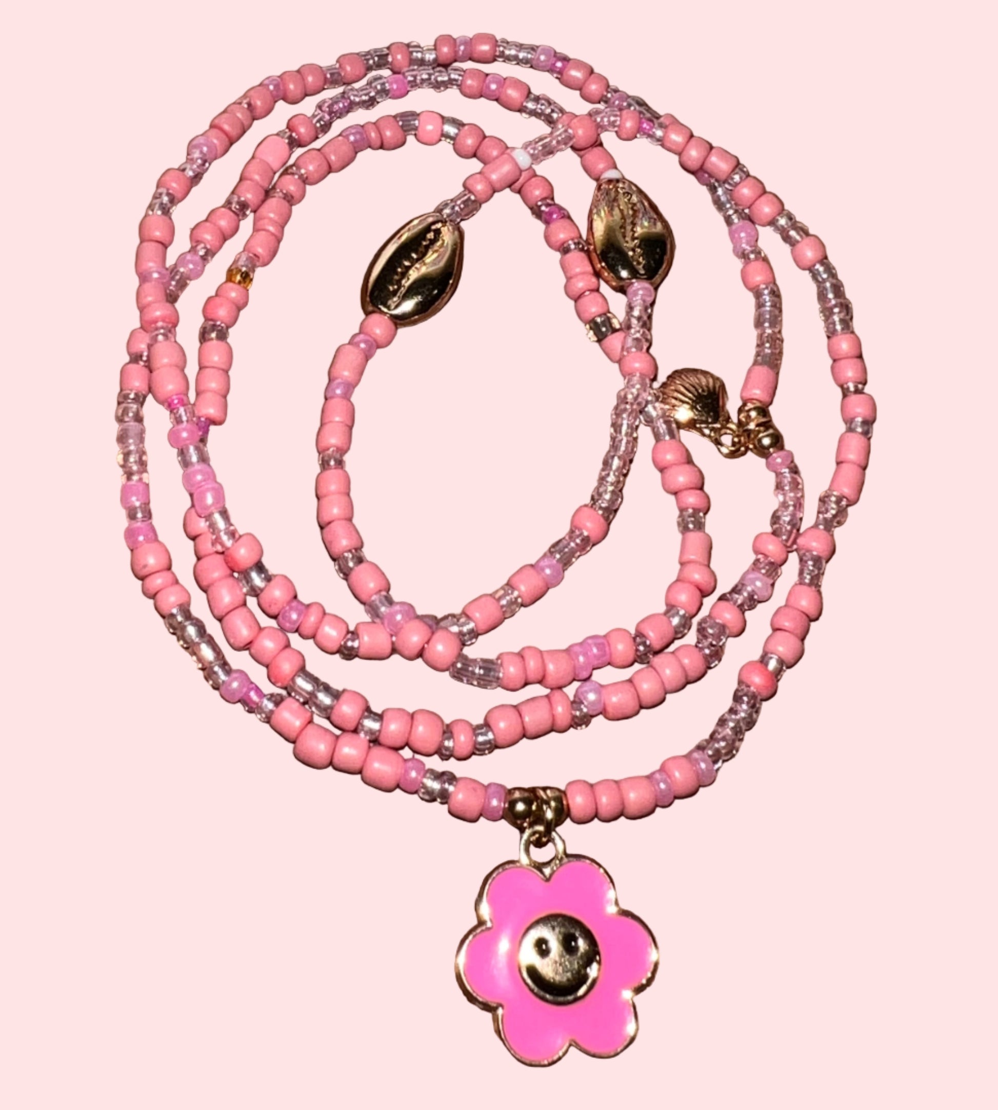 Pink beaded waistbeads with a flower pendant on a wooden surface