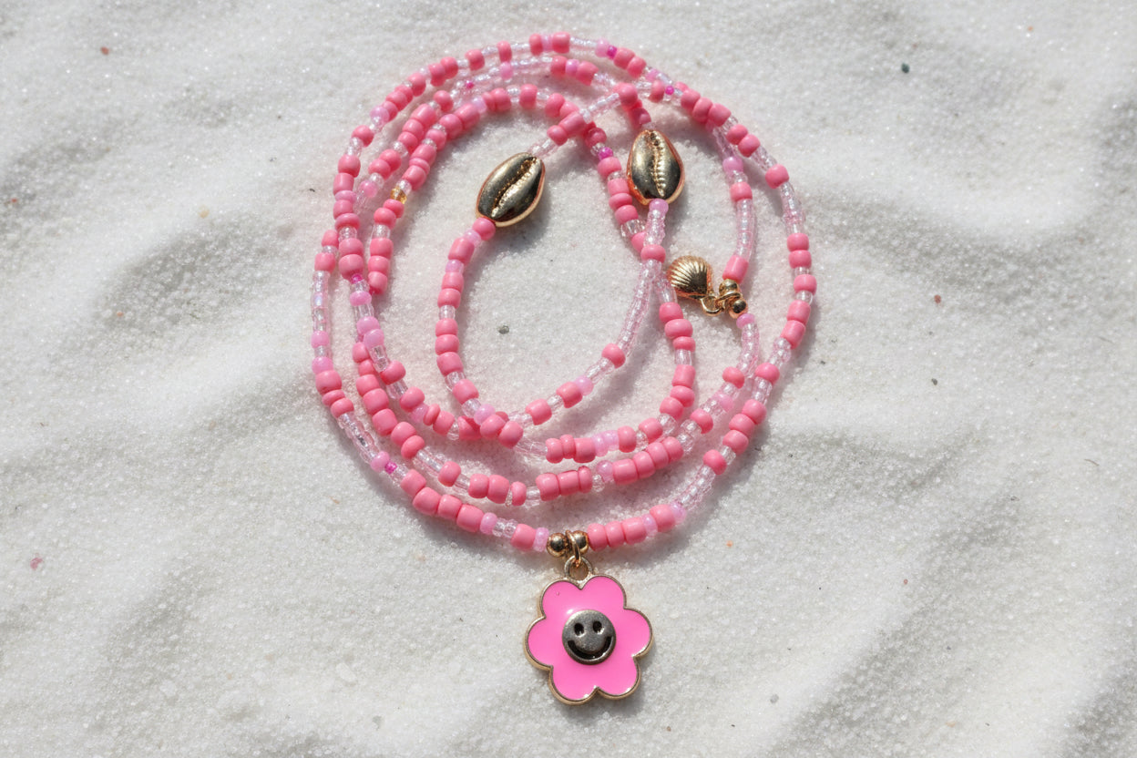 Pink beaded waistbeads with a flower pendant on a wooden surface