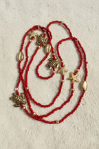 Red waistbeads with gold turtle and starfish charms on a white sand background