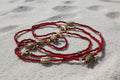 Red waistbeads with gold turtle and starfish charms on a white sandbackground