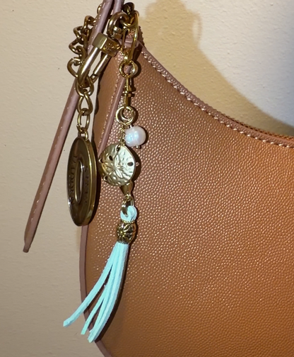 Handbag with decorative charm featuring an aqua tassle, gold sand dollar, freshwater pearl