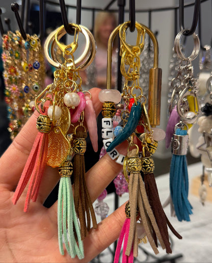 Collection of colorful repurposed purse chains or keychains with tassels in front of a display stand.