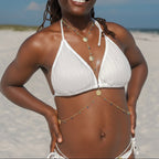 Woman in a white bikini standing on a sandy beach with a blue sky.