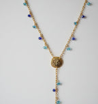 A gold-toned lariat-style necklace with two textured circular medallion sand dollar pendants and small blue bead accents