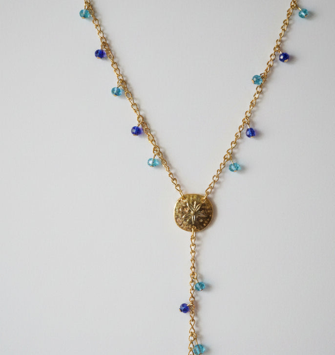 A gold-toned lariat-style necklace with two textured circular medallion sand dollar pendants and small blue bead accents