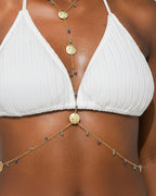 Woman in a white bikini standing on a sandy beach with a clear sky.