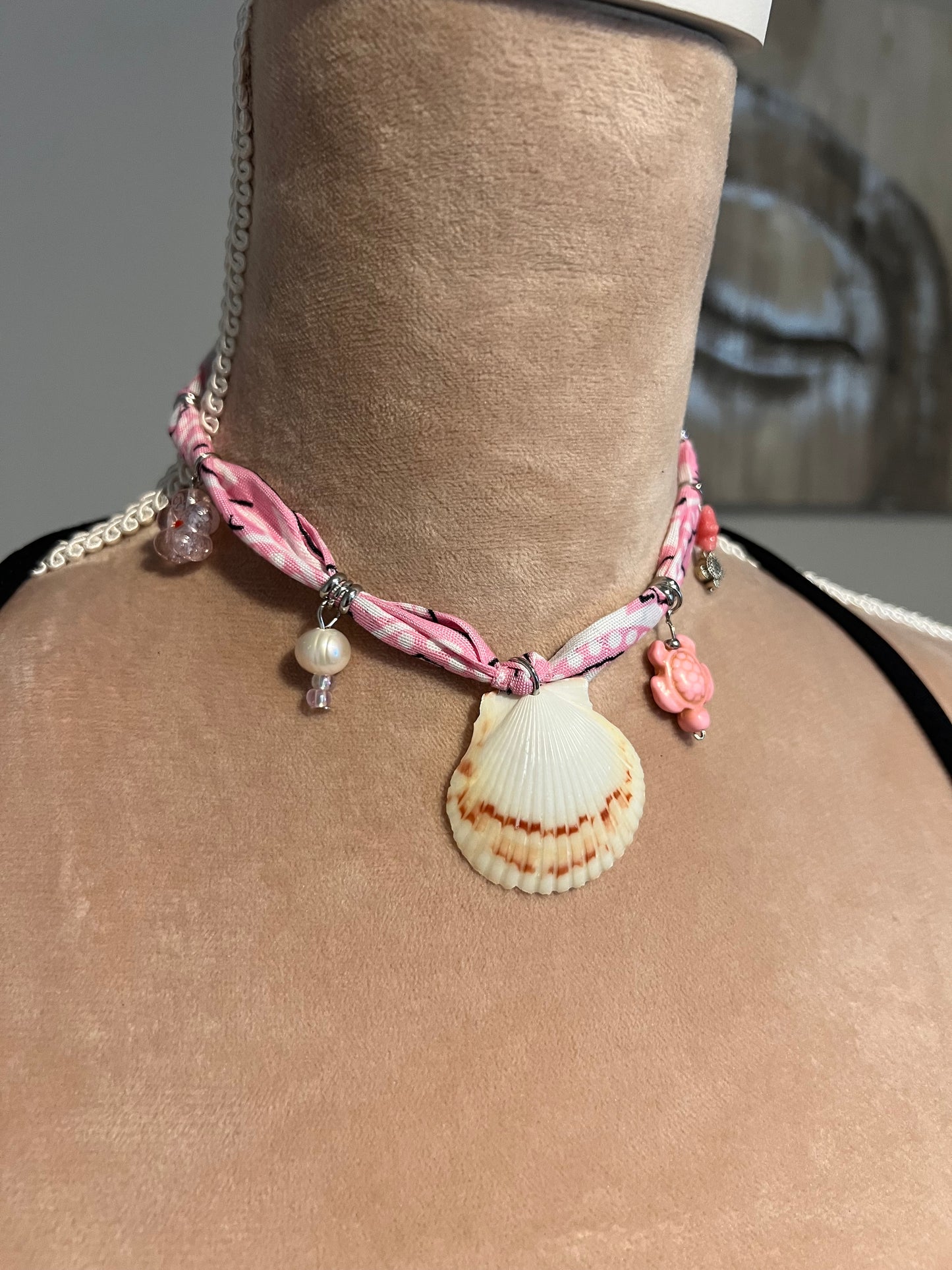 bandana necklace with shell and pearl charm on a person's neck against a neutral background