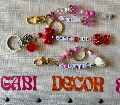 Decorative keychains with various charms and shells on a textured surface with 'gAbI DECOR' branding.