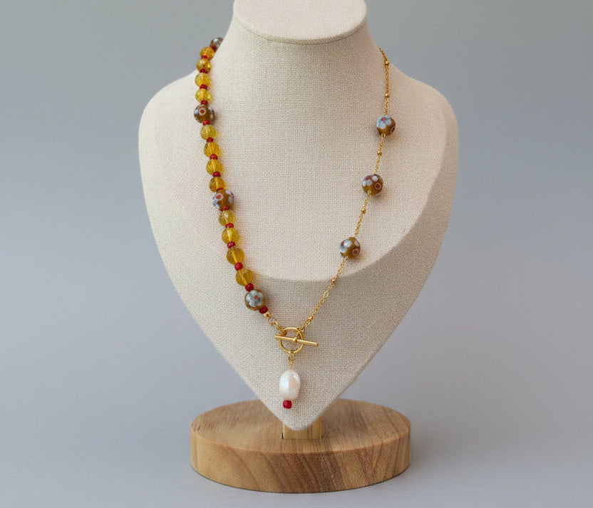 A gold-tone beaded necklace with amber, brown, and red beads displayed on a jewelry bust