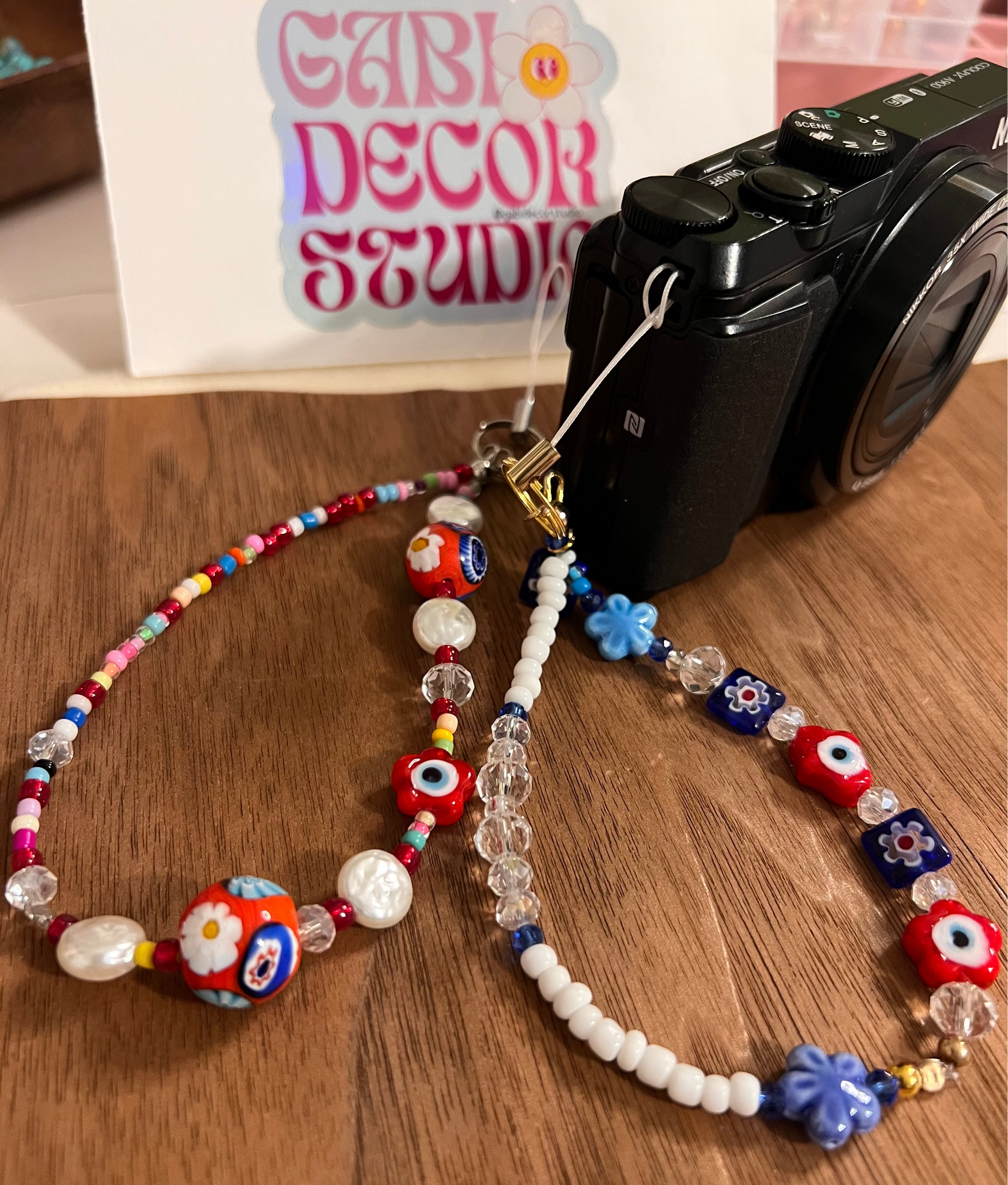 Colorful beaded camera strap on a wooden surface with 'Gabi Decor Studio' in the background.